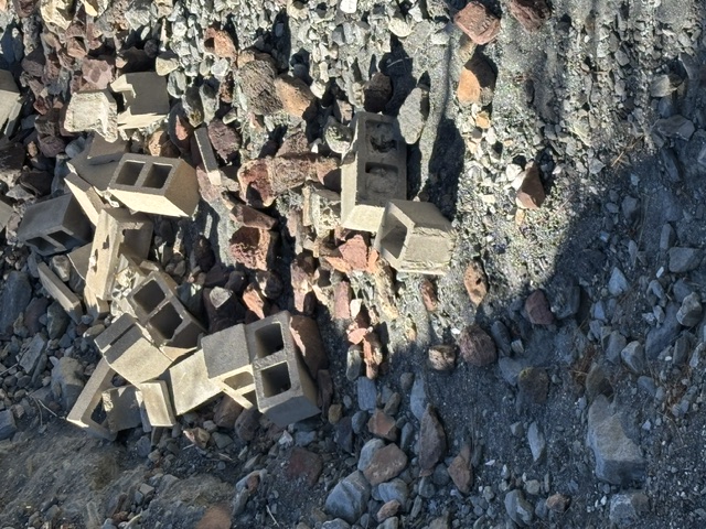 Broken cinder blocks and rubble dumped along a hillside