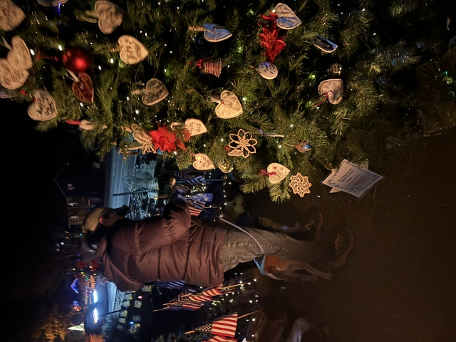 A holiday tree decorated with handwritten heart ornaments beside American flags at night