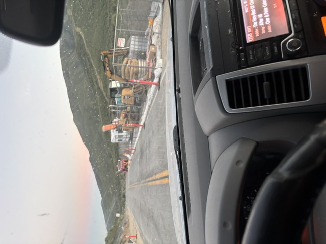 Heavy equipment and pipe staged for infrastructure work beside a mountain highway